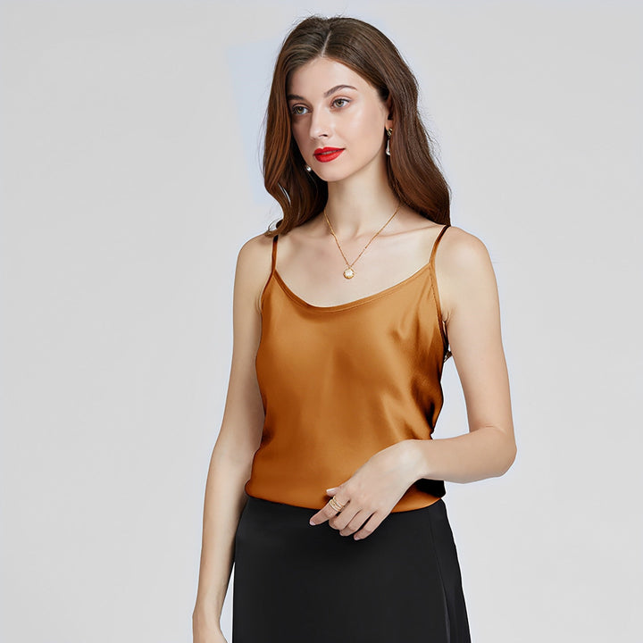 A woman with long brown hair wears a SusanSilk Classic Round Neck Silk Camisole in gold and a black skirt, standing against a plain light background.