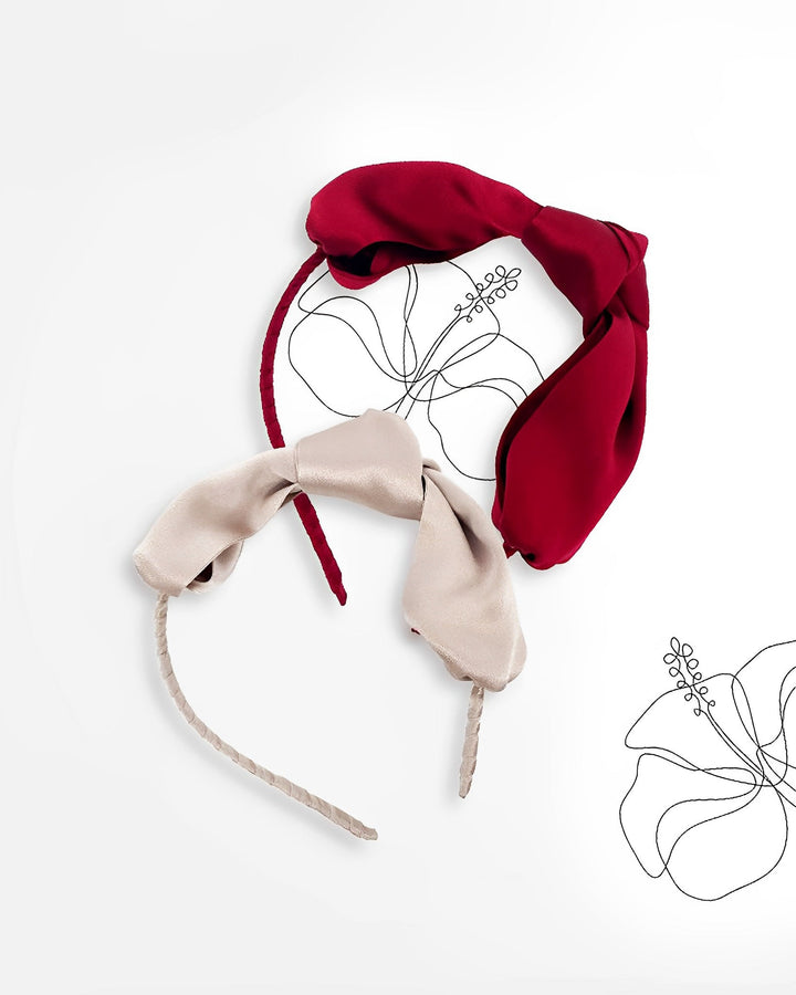 Two Pure Color Bow Knot Silk Headbands from SusanSilk, one in red and one in beige, are displayed on a white surface with black floral outlines in the background. These elegant accessories add a touch of sophistication to any outfit.