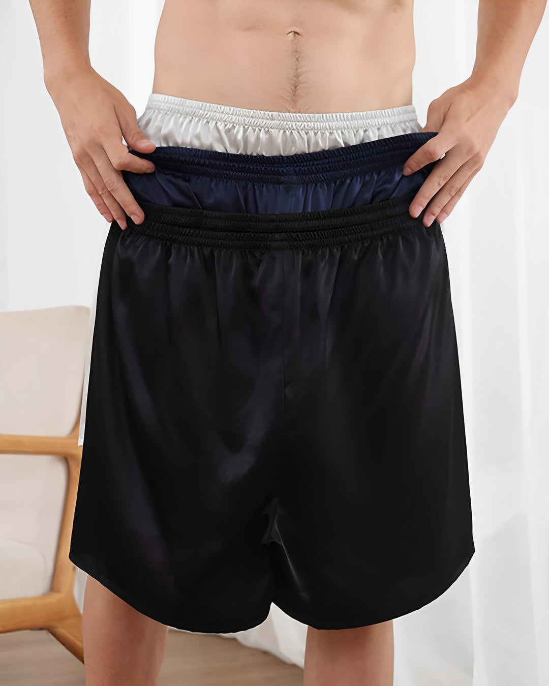 A person is wearing a pair of 19 Momme Comfortable Silk Boxers from SusanSilk while holding up the waistband to reveal three additional layers of different colored silk waistbands underneath.