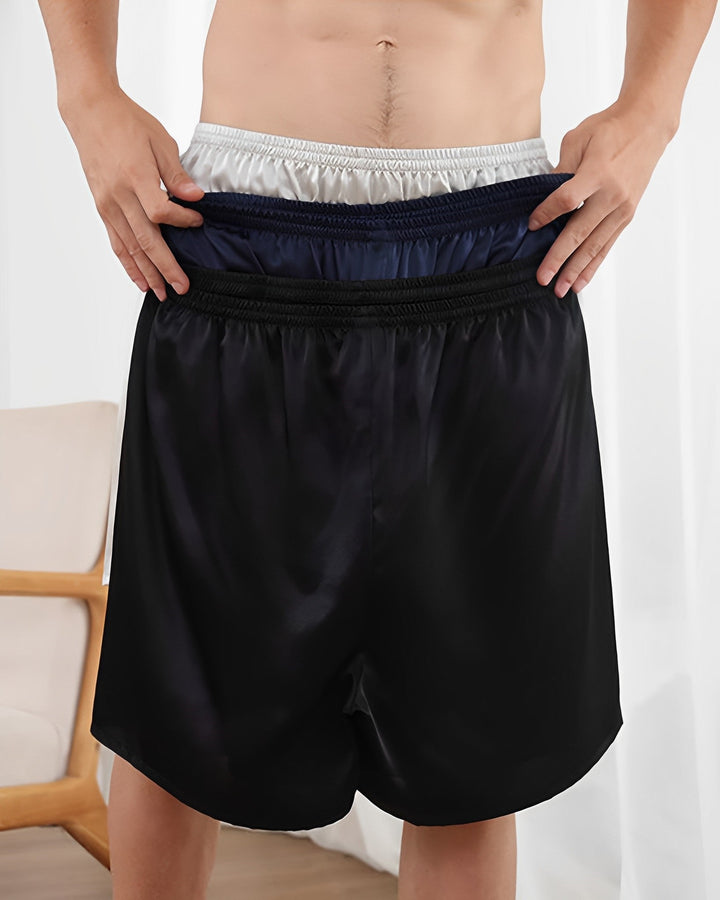 A person is wearing a pair of 19 Momme Comfortable Silk Boxers from SusanSilk while holding up the waistband to reveal three additional layers of different colored silk waistbands underneath.
