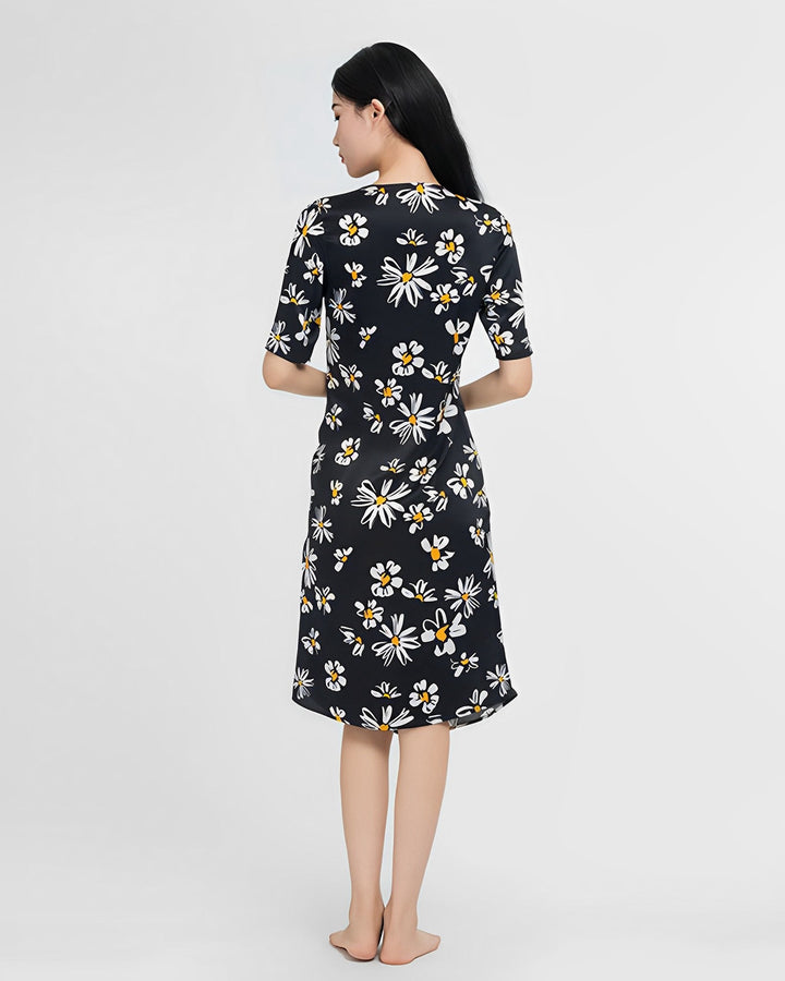 A person with long black hair stands barefoot, facing away, wearing a Stylish Overlapping Floral Silk Dress by SusanSilk adorned with a white and yellow daisy print.