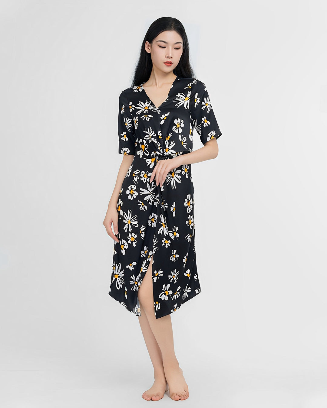 A person with long dark hair stands barefoot, wearing a Stylish Overlapping Floral Silk Dress by SusanSilk with a front slit, against a plain background.