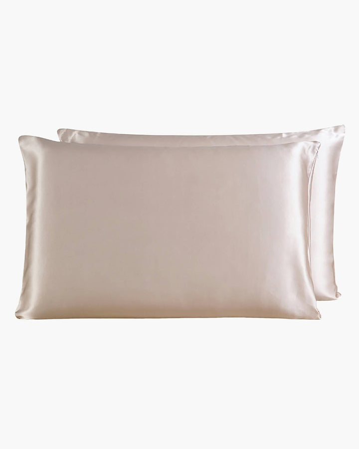 Two elegant 22 Momme Beauty Silk Pillowcases Zipper from SusanSilk in a soft beige hue are artfully placed one in front of the other against a pristine white background.