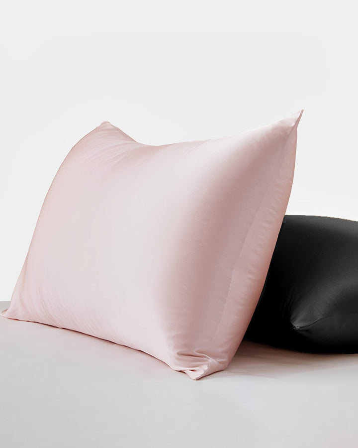 A 22 Momme Beauty Silk Pillowcase Zipper in pink, from the luxurious SusanSilk collection, is displayed in front of a black satin pillowcase on a pristine white surface.