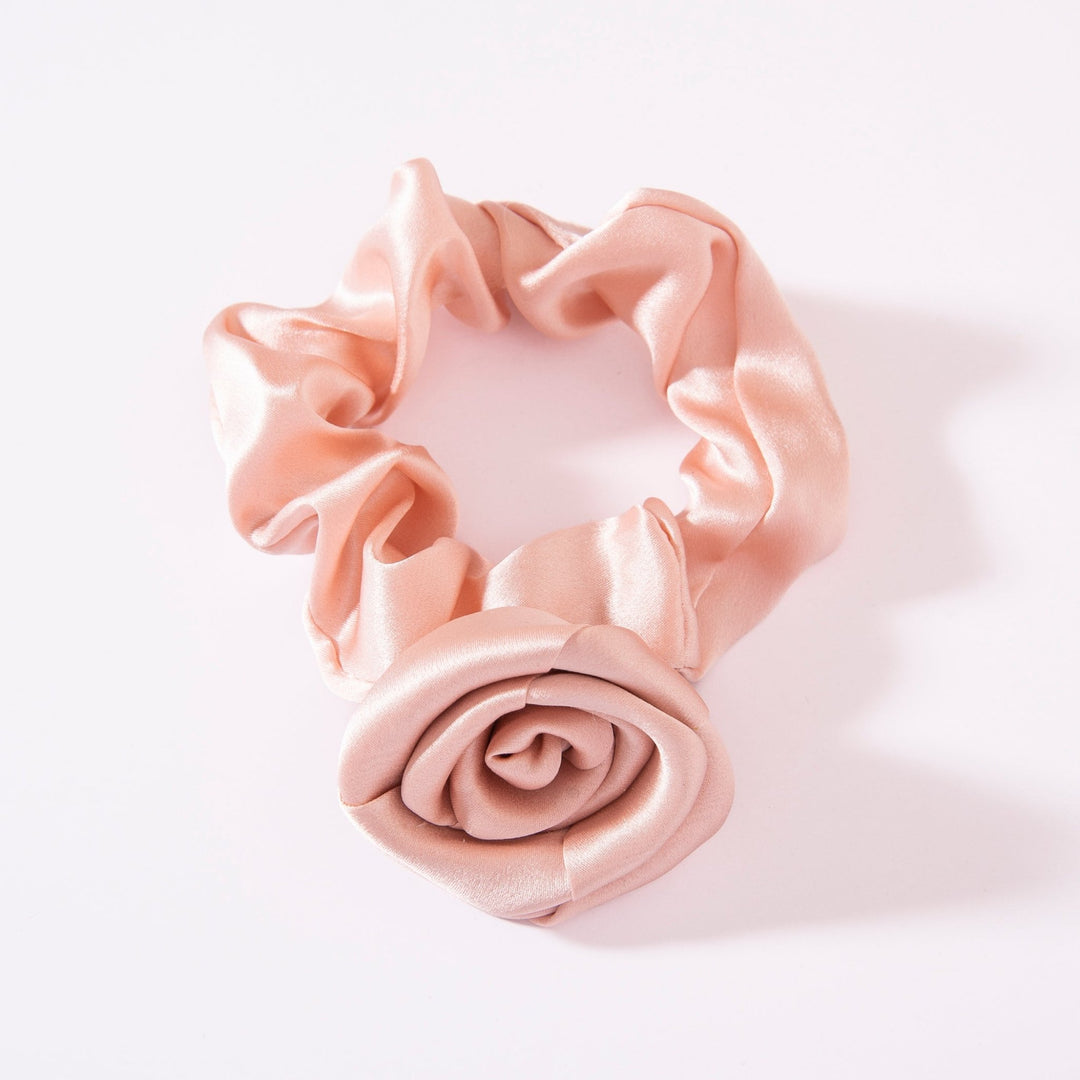 The Elegant Camellia Silk Scrunchie by SusanSilk features a light pink satin design with a rose-shaped embellishment, crafted from luxurious silk, set against a white background.