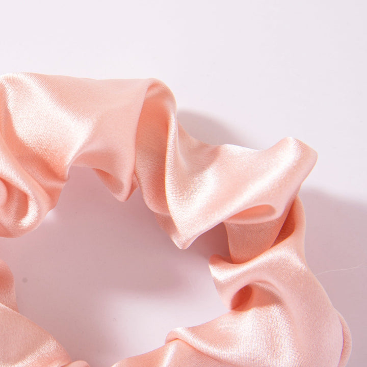 A close-up of the Elegant Camellia Silk Scrunchie from SusanSilk, featuring light pink satin, against a white background.