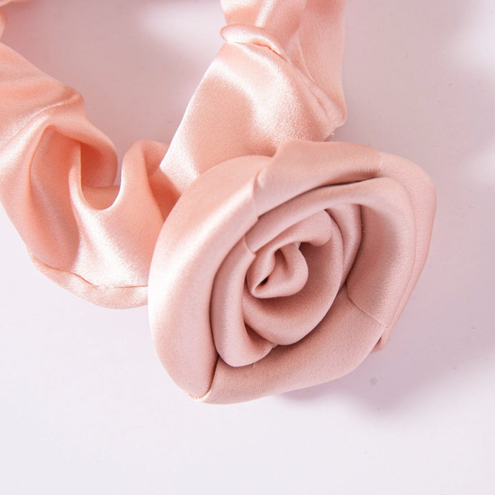 A close-up of the Elegant Camellia Silk Scrunchie by SusanSilk, crafted from peach-colored silk satin and elegantly designed in the shape of a rose.