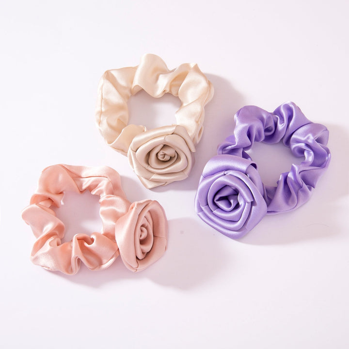 Three Elegant Camellia Silk Scrunchies by SusanSilk in soft pink, cream, and lavender are arranged on a white background. Each scrunchie features a rose-shaped design.