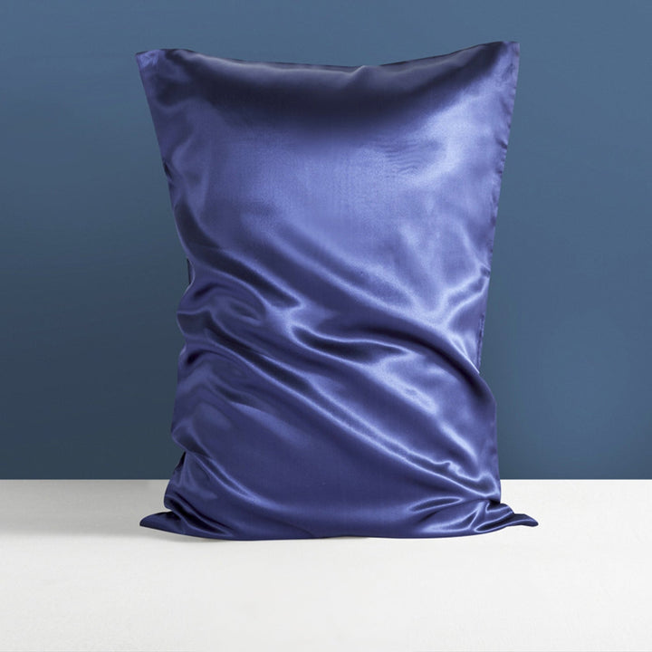 A luxurious 22 Momme High Gloss Silk Pillowcase Envelope in blue, crafted by SusanSilk, is shown against a two-tone wall background.