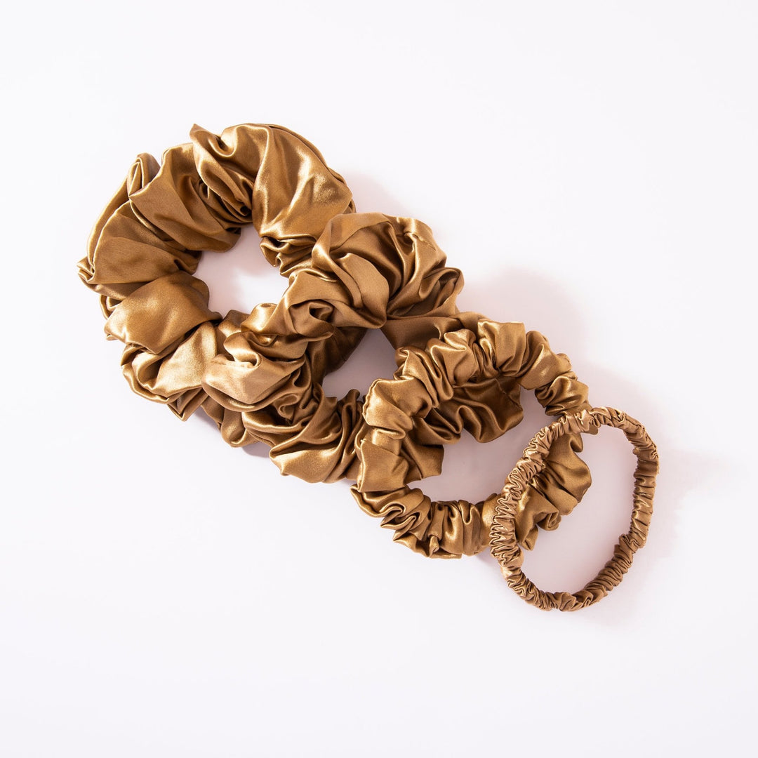 Three gold-colored scrunchies of varying sizes, crafted from luxurious silk by SusanSilk, are displayed on a white background. This set is part of their 22 Momme Luxury Silk Scrunchies 4-Pack collection.