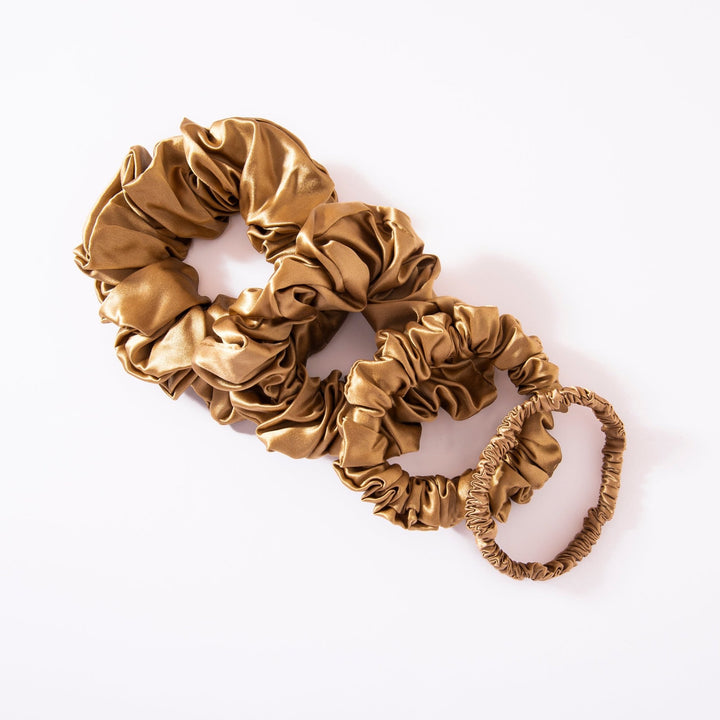 Three gold-colored scrunchies of varying sizes, crafted from luxurious silk by SusanSilk, are displayed on a white background. This set is part of their 22 Momme Luxury Silk Scrunchies 4-Pack collection.
