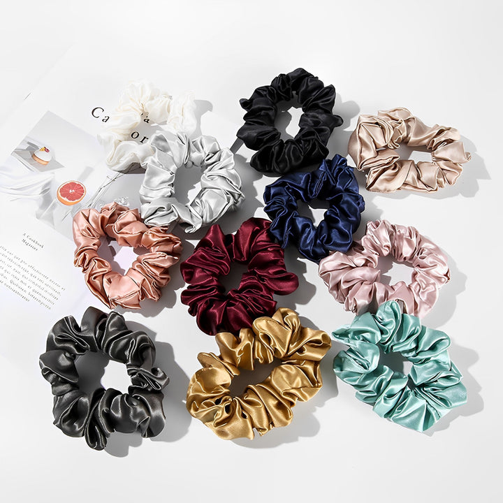 A set of four SusanSilk 22 Momme Luxury Silk Scrunchies in various colors, arranged in a flat lay pattern on a white surface, next to a magazine.