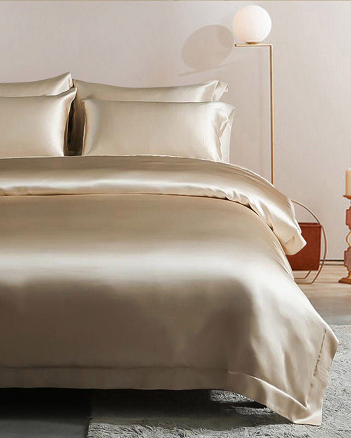A neatly made bed with a SusanSilk 22 Momme Seamless Silk Duvet Cover in beige with flange border, complemented by matching pillows in a minimalist bedroom featuring a modern floor lamp and a side table.