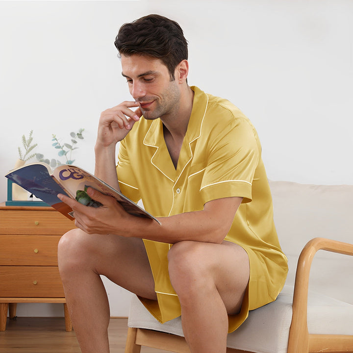 A man in a SusanSilk 22 Momme Short Silk Pajamas Set sits on a chair, reading a magazine.