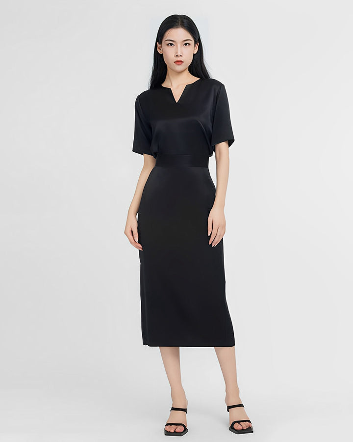 A person stands wearing a short-sleeved, black Elegant Two-Piece Silk Dress Set by SusanSilk and black heels against a plain white background.