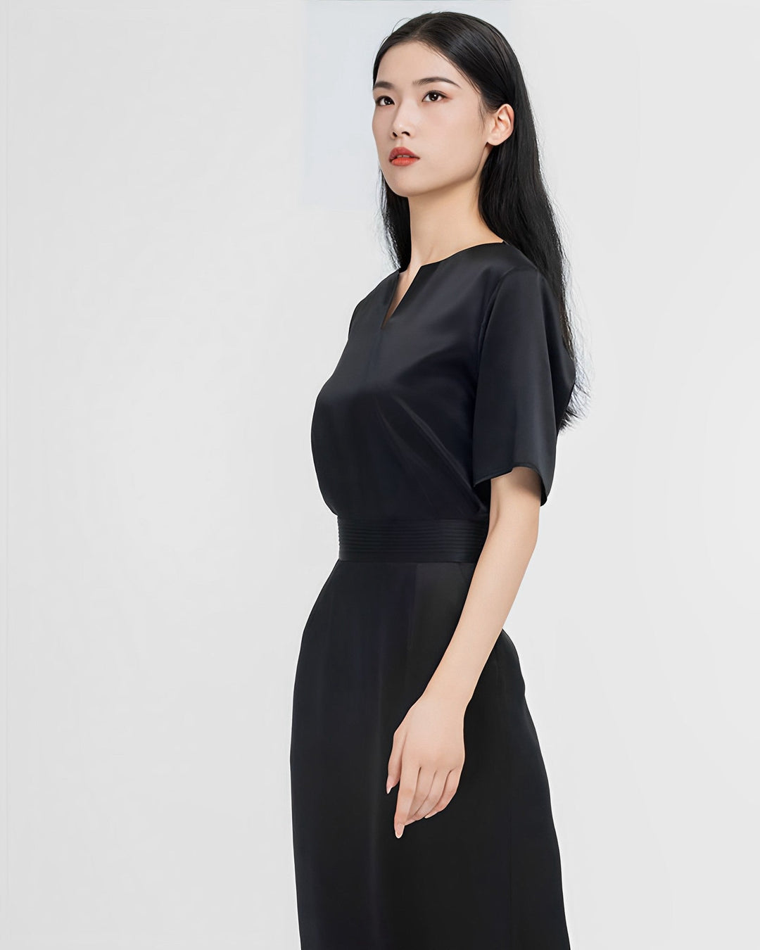 A woman with long black hair is standing and looking slightly to the side. She is wearing the Elegant Two-Piece Silk Dress Set from SusanSilk. The background is plain white.