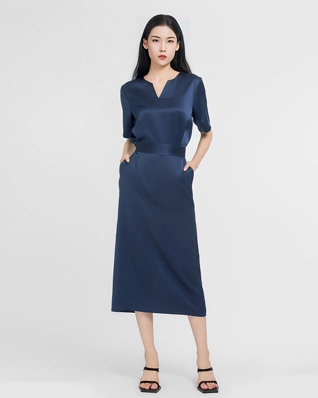 A person wearing an Elegant Two-Piece Silk Dress Set by SusanSilk in navy blue and black sandals stands against a plain white background with hands in pockets.