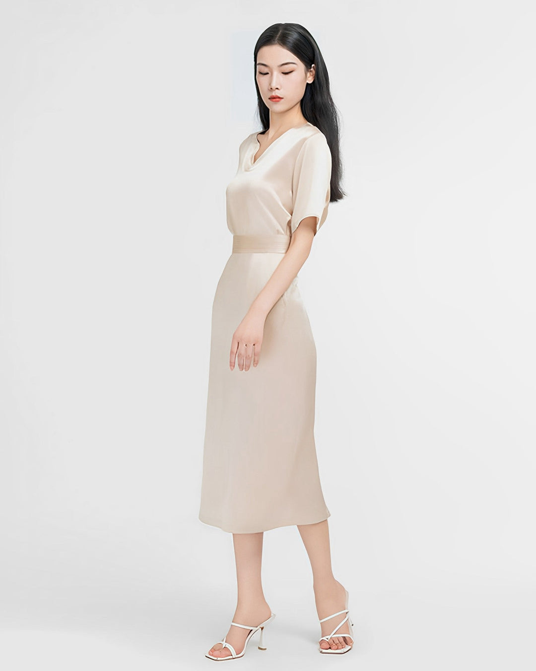 A woman stands with her left hand by her side and her right hand extended slightly, wearing a beige, short-sleeve **Elegant Two-Piece Silk Dress Set** from **SusanSilk**. She completes her look with white high-heeled sandals against a plain white background.