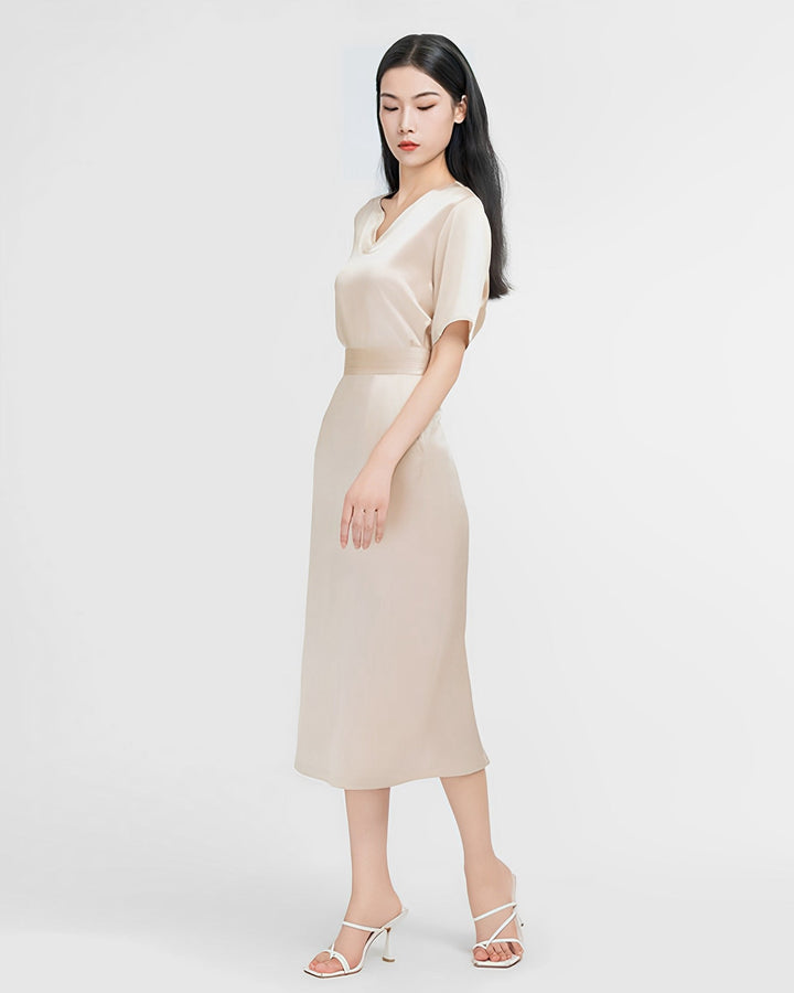 A woman stands with her left hand by her side and her right hand extended slightly, wearing a beige, short-sleeve **Elegant Two-Piece Silk Dress Set** from **SusanSilk**. She completes her look with white high-heeled sandals against a plain white background.
