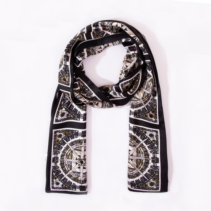 A black and white Black Compass Narrow Long Silk Scarf from SusanSilk, featuring intricate geometric designs, is neatly folded on a white background.