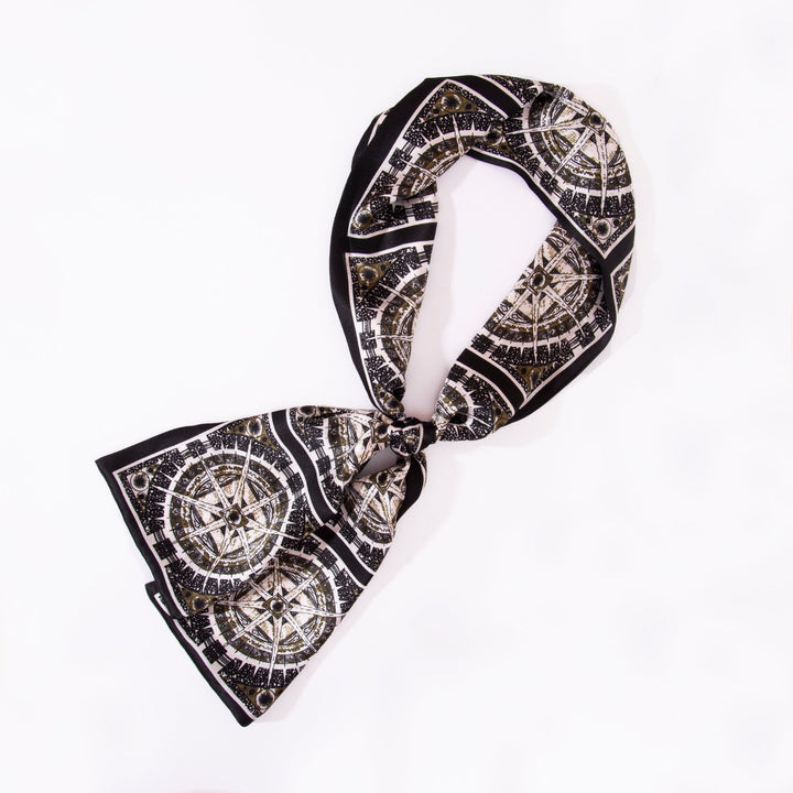 A Black Compass Narrow Long Silk Scarf from SusanSilk is tied in a loose knot against a plain white background.