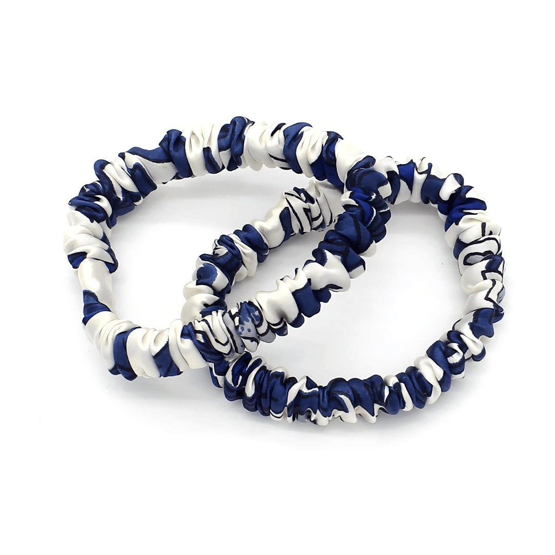 Two intertwined scrunchies from the SusanSilk Celadon Print Silk Scrunchies Set 3-Pack, featuring a white and navy blue marbled pattern.