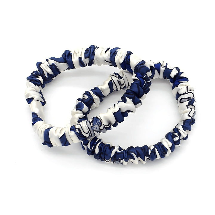 Two intertwined scrunchies from the SusanSilk Celadon Print Silk Scrunchies Set 3-Pack, featuring a white and navy blue marbled pattern.