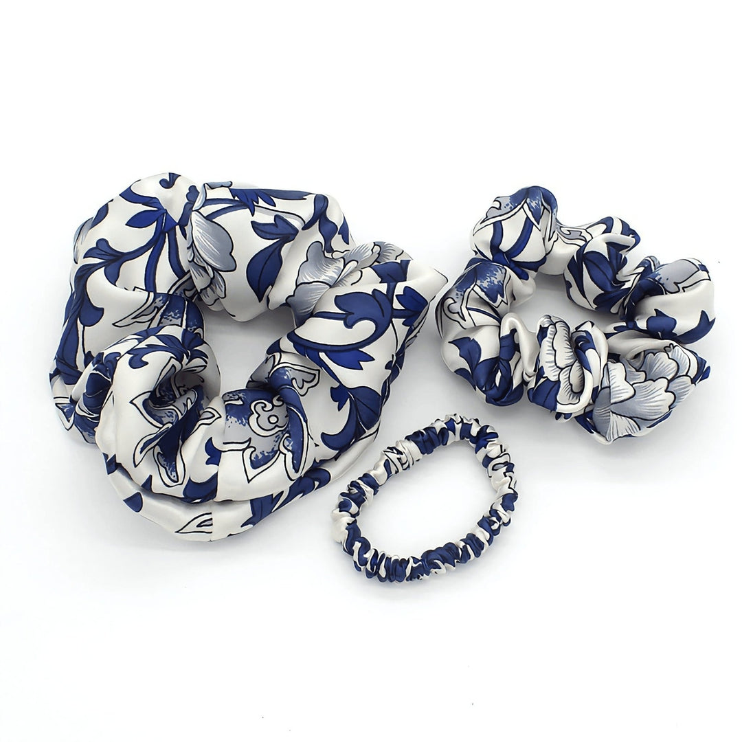 Three elastic hair scrunchies from the SusanSilk Celadon Print Silk Scrunchies Set 3-Pack, featuring luxurious silk with white and blue floral patterns, are arranged against a white background.