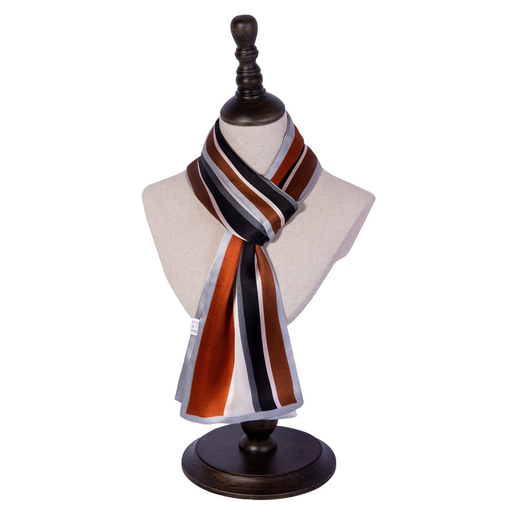 A mannequin displays a SusanSilk Color Strips Narrow Long Silk Scarf, featuring brown, black, white, and silver hues. The scarf is draped neatly to showcase its design while the mannequin stands on a wooden stand.