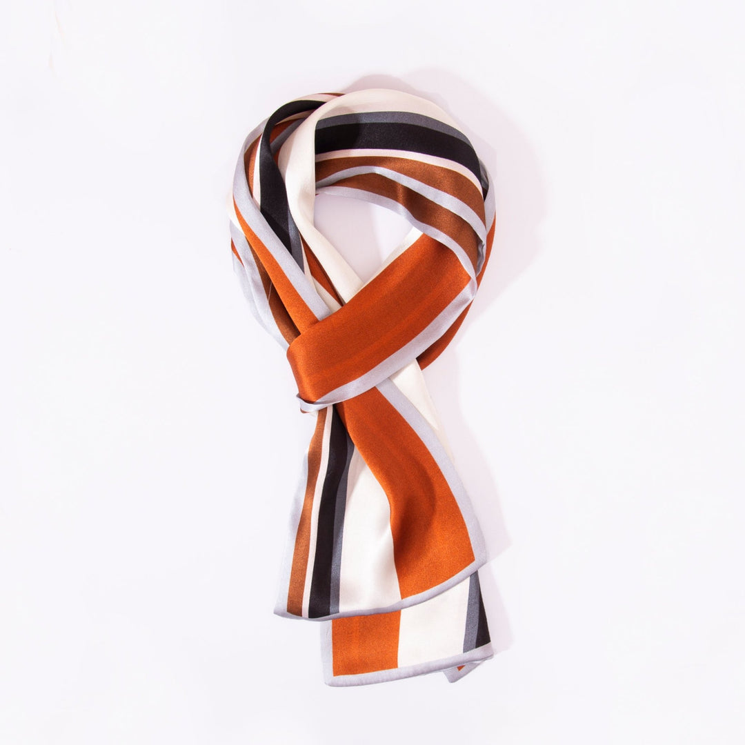 A neatly folded Color Strips Narrow Long Silk Scarf from SusanSilk, featuring bold stripes in white, orange, black, and brown.
