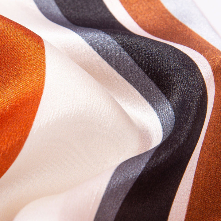 Close-up image of the luxurious SusanSilk Color Strips Narrow Long Silk Scarf, showcasing its smooth texture and diagonal stripes in shades of orange, white, and black.