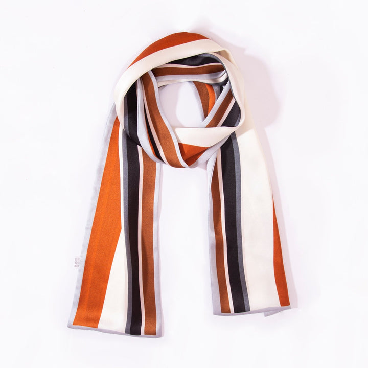 A Color Strips Narrow Long Silk Scarf by SusanSilk featuring vertical stripes in orange, black, white, and brown colors set against a plain white background.