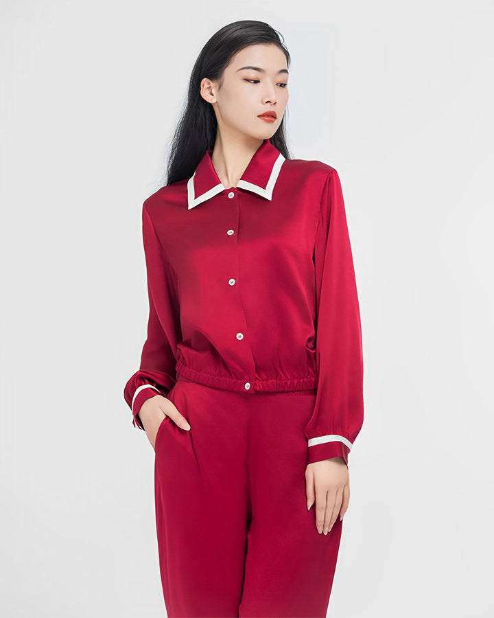 A person stands against a white background, wearing the SusanSilk French Vintage Style Red Silk Pajamas Set, featuring white trim on the collar and cuffs. One hand is in their pocket as they look to the side.