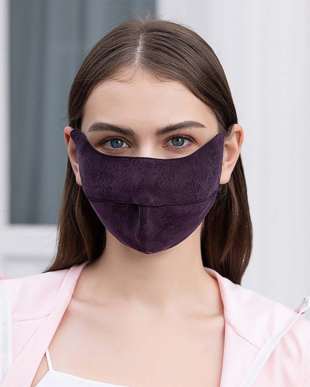 A person with long hair is wearing a purple SusanSilk face mask and a light-colored jacket, the background blurred. The Jacquard Cloche Hat & Face Mask fabric glistens like silk.
