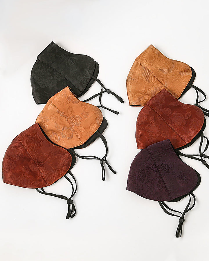 A set of six Jacquard Cloche Hat & Face Masks by SusanSilk, featuring intricate patterns in black, orange, red, and purple hues, elegantly arranged in semi-circular rows on a white background.