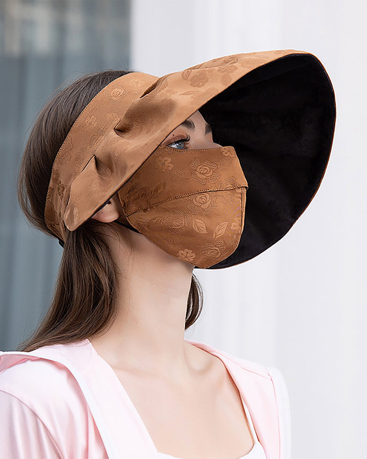 A person wearing the Jacquard Large Brim Hat and matching Face Mask by SusanSilk looks to the side. The indoor background features a window with curtains partly visible, hinting at the elegant touch of susansilk fabric in the scene.