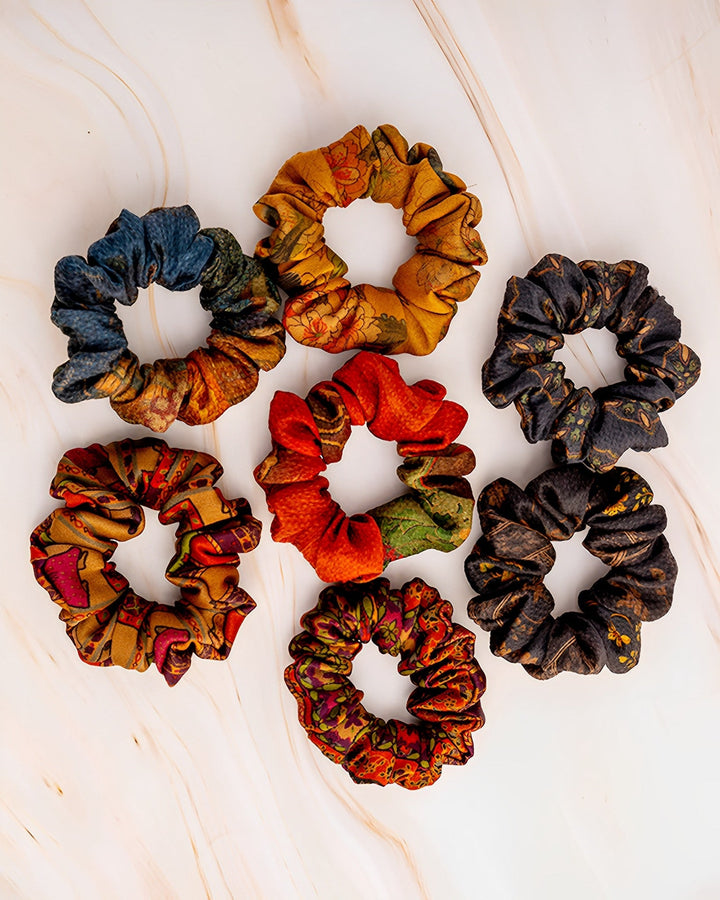 A set of SusanSilk's Gambiered Canton Gauze Silk Scrunchies, measuring 5cm, displayed in a circular pattern on a light marbled surface.