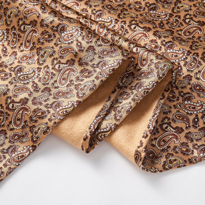 A close-up of the Paisley Long Silk Brushed Scarf - Gold by SusanSilk, showcasing its paisley pattern in shades of brown, yellow, and red. The luxurious silk is slightly folded.