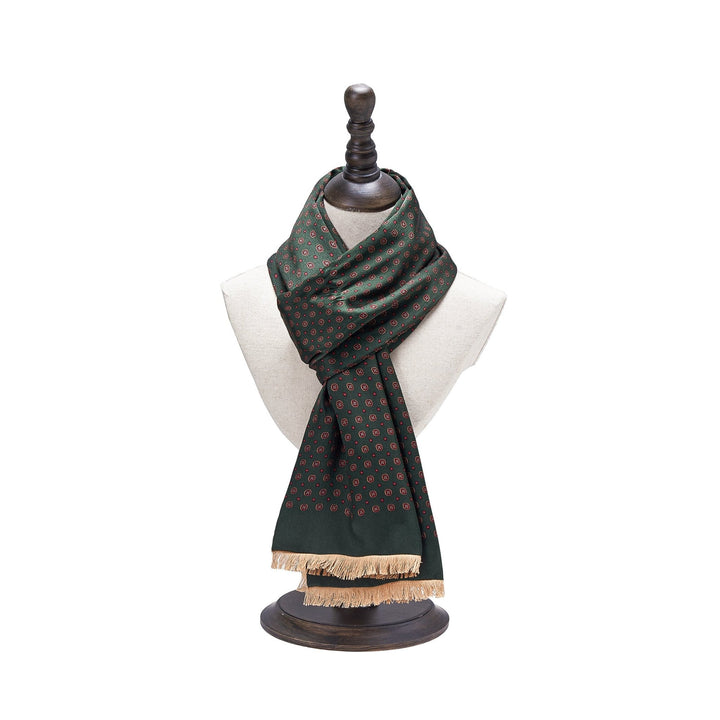 The SusanSilk Geometric Pattern Long Silk Brushed Scarf in green is exhibited on a white mannequin with a dark wooden stand, showcasing its beige fringes.