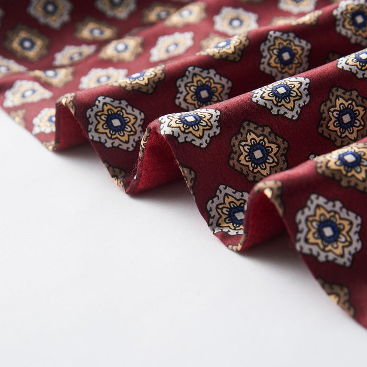 Close-up of the Geometric Pattern Long Silk Brushed Scarf - Red by SusanSilk, showing folded fabric featuring blue, white, and brown diamond-shaped designs against a red background.