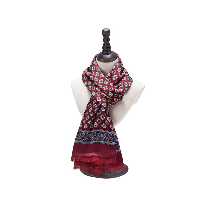 A mannequin displays the SusanSilk Geometric Pattern Long Silk Brushed Scarf in red, adorned with blue and white details and fringed edges. The scarf is draped loosely around the neck.