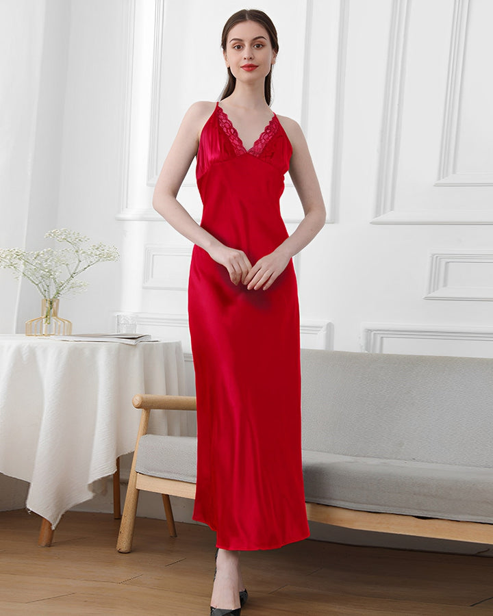A woman in a red, sleeveless, V-neck Lace Long Silk Nightdress by SusanSilk is standing indoors. The room has white walls, a table with a vase of flowers, and a beige bench.