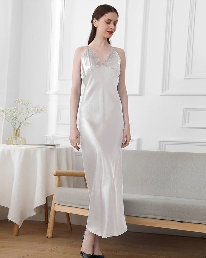 A woman in a sleeveless, ankle-length Lace Long Silk Nightdress by SusanSilk stands next to a bench against a white wall with decorative molding.