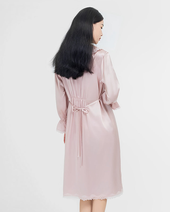 A woman with long black hair in a light pink SusanSilk Premium Lace Silk Nightdress stands with her back to the camera against a plain white background.