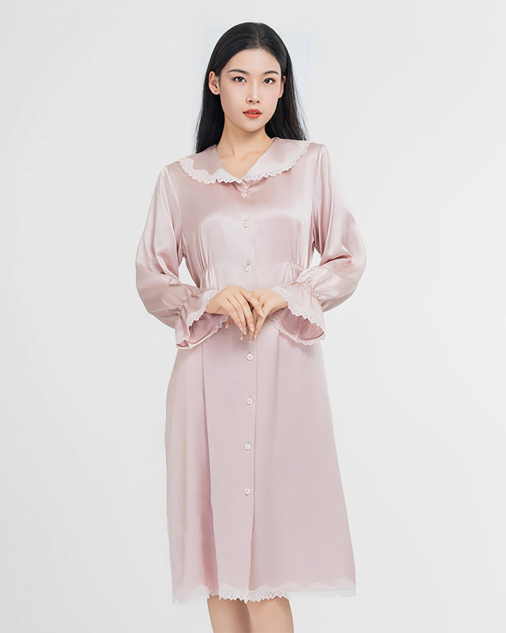 A woman stands facing forward wearing a light pink button-up Premium Lace Silk Nightdress with delicate lace trim on the collar, cuffs, and hem. The elegant gown from SusanSilk appears to be made from luxurious materials, adding a touch of sophisticated charm.