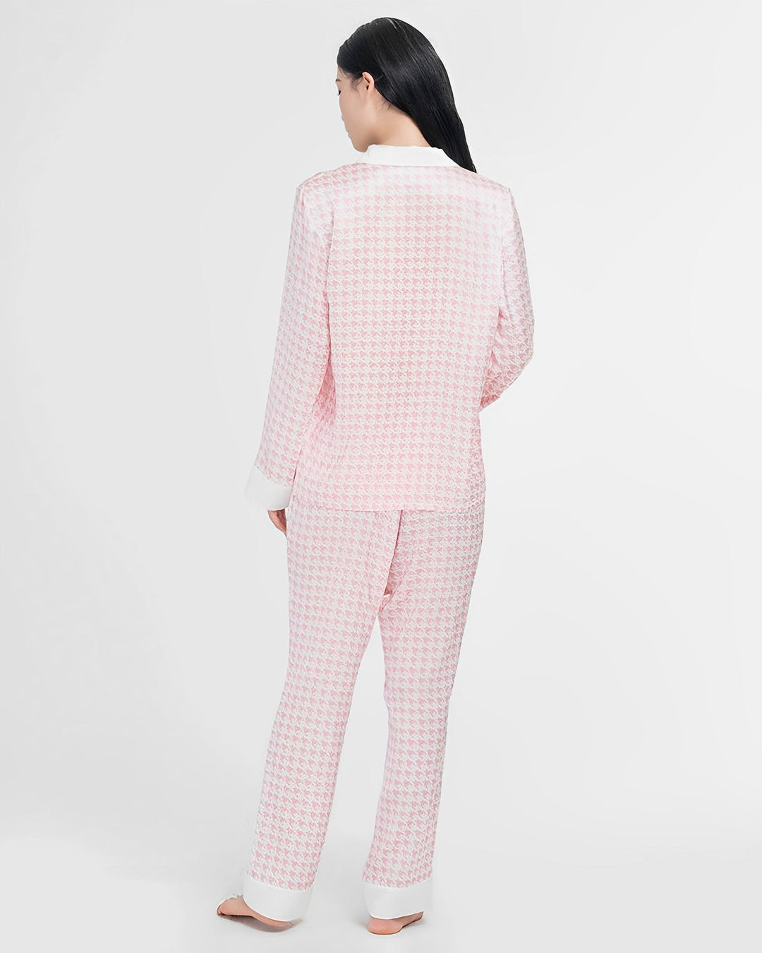 A person with long black hair is standing barefoot and facing away, wearing the Houndstooth Silk Pajamas Set from SusanSilk.