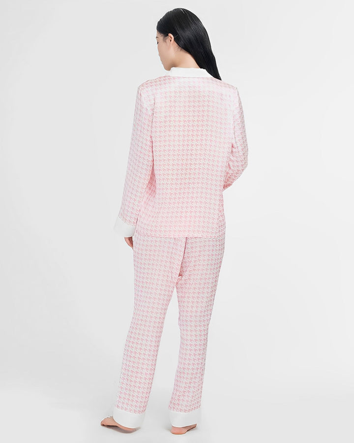 A person with long black hair is standing barefoot and facing away, wearing the Houndstooth Silk Pajamas Set from SusanSilk.