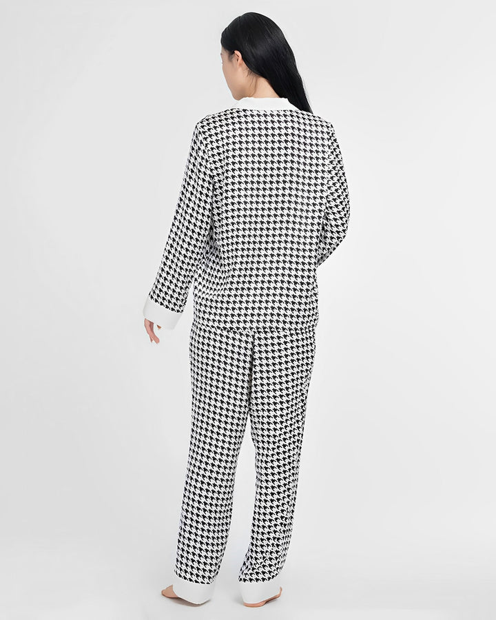 A person stands facing away from the camera, dressed in a matching SusanSilk Houndstooth Silk Pajamas Set, featuring a black-and-white houndstooth pattern and crafted from luxurious silk.