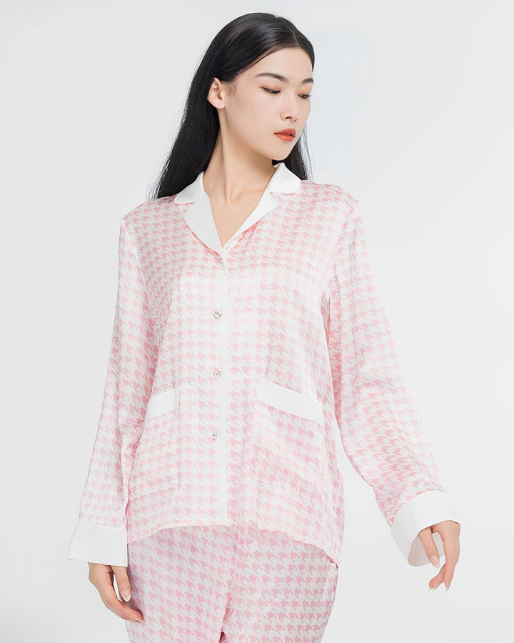 A woman with long black hair is wearing the SusanSilk Houndstooth Silk Pajamas Set, featuring a pink and white houndstooth button-up top and matching pants made from luxurious silk, against a plain white background.
