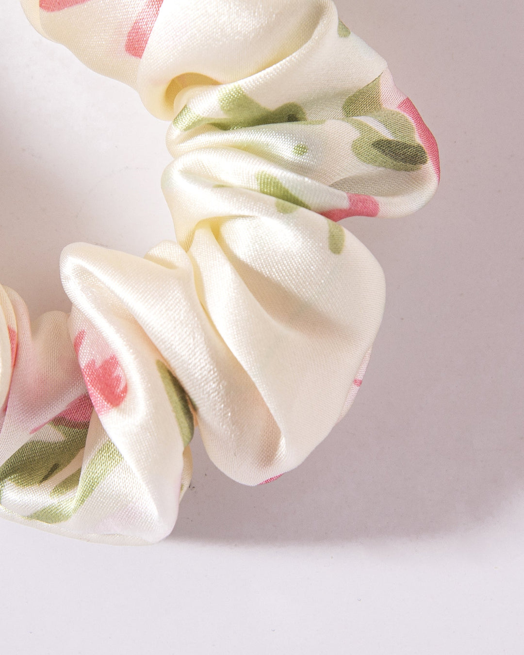 Close-up of a scrunchie from the SusanSilk Lovely Flowers Silk Scrunchies Set 3-Pack, made from white silk fabric adorned with pink and green floral patterns, set against a white background.